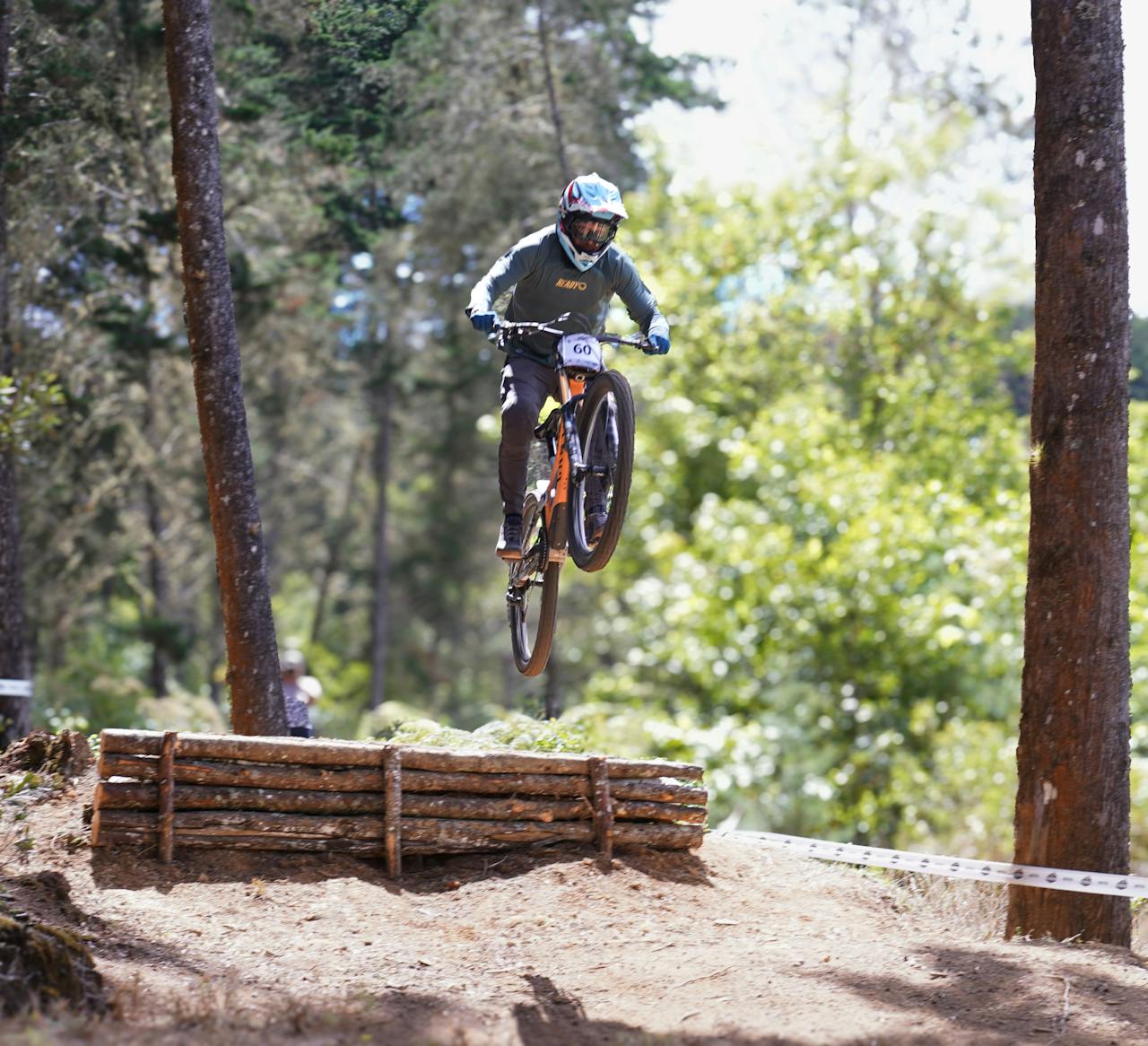 Mountain biker performs a jump over a wooden obstacle on a forest trail in Costa Rica, captured mid-air.